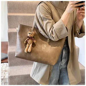 Detail of a brown patchwork tote bag with a knitted bear charm and textured finish