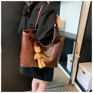 Detailed view of dark brown tote bag with contrast stitching and knit bear charm