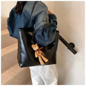Detail of black tote bag with square quilted texture and brown bear charm on shoulder