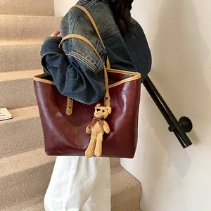 Large burgundy patchwork tote bag with light brown straps and a yellow plush bear pendant