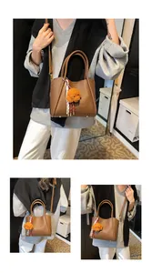 Detail view of brown lychee grain leather bucket bag with puppy charm and striped ribbon