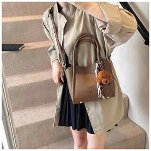 Brown litchi grain bucket bag with cute teddy pendant and embossed lettering detail