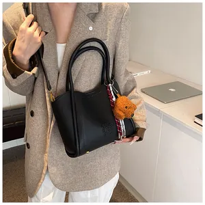 Detail of black lychee texture bucket bag with plush bear charm and gold hardware