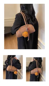 Detail of a brown leather shoulder bag featuring a teddy bear charm and plaid ribbon accent