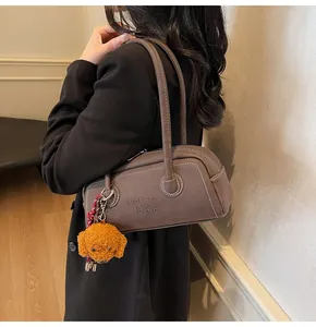 Detail of brown faux leather Boston bag with stitching and plush dog charm on shoulder
