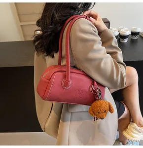 Detail of vintage reddish cylinder bag with white stitching and teddy bear charm accessory