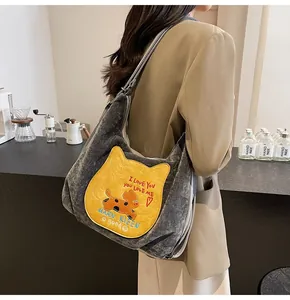 Détail du sac à bandoulière en velours gris avec patch chat jaune et bandoulière rayée au café