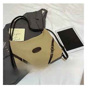 Detail of large khaki tote bag with dark brown trim and gold hardware on white bed
