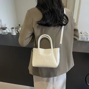 Weiße Eimertasche mit Webmuster, Tragegriffen und abnehmbarem Schultergurt im Café