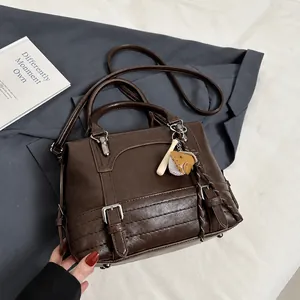 Detail van donkerbruine PU-lederen handtas met honkbalbedel op een grijze blazer