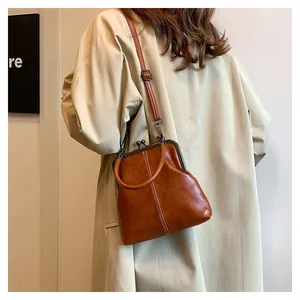 Brown oil wax leather handbag with retro metal frame clasp worn over a beige trench coat