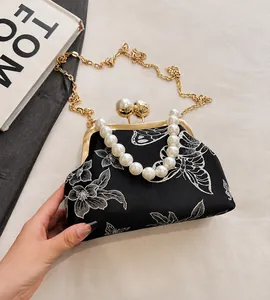 Detalle del bolso vintage negro con bordado floral y asa grande de perlas blancas
