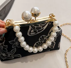 Detalle de bordado en bolso negro con asa de perlas y cierre metálico dorado