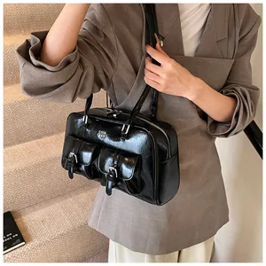 Detail of black patent leather shoulder bag with buckle pockets and retro workwear style
