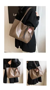 Detail of a brown leather tote bag with a plush doll charm and striped strap accent