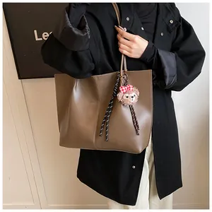 Detail of a brown leather tote bag with a plush bear charm and vertical seam decoration