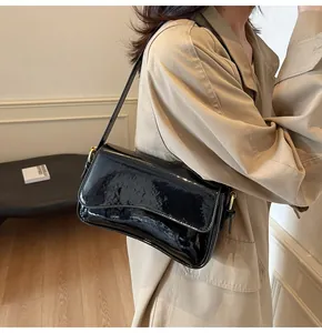 Detail of black glossy patent leather shoulder bag with adjustable gold buckle on strap