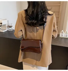 Detail of a dark brown glossy patent leather crossbody bag with curved flap design