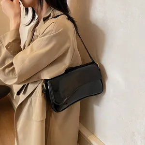 Elegant black patent leather shoulder bag with magnetic flap worn by a model in a trench coat