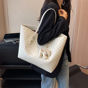 Bolso tote beige con estampado de monograma y amuleto de perro mostrado por una modelo