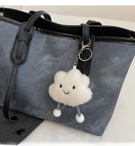 Close-up of a white fluffy cloud plush keychain hanging on a blue denim tote bag