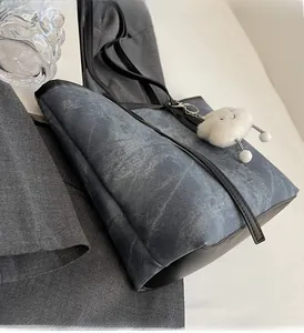 Detail of blue denim tote bag with black leather trim and white cloud charm accessory