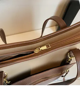 Detailaufnahme der glatten goldenen Metallreißverschlüsse an einer braun-beigen Tasche