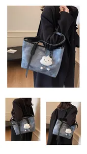 Detail of large denim tote bag with black leather handles and white cloud plush charm