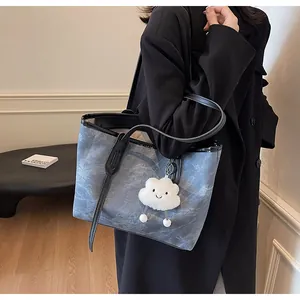 Detail of blue denim tote bag with black leather straps and a plush cloud charm