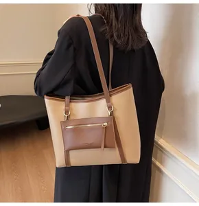 Detalle de un bolso tote grande beige con un sobre pequeño y letras de moda laterales