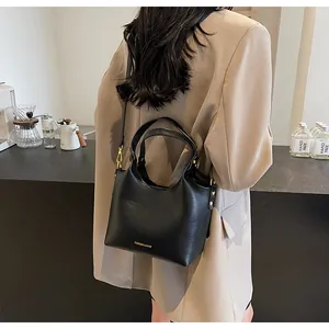 Mannequin portant un sac seau noir mat avec lettrage doré dans un décor de café