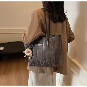 Detail view of large dark brown tote bag with vintage texture and plush pendant