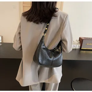 On-body shot of a black crescent hobo bag with glossy leather and gold hardware
