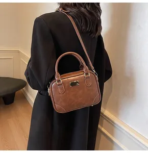 Detailed side view of vintage brown leather crossbody bag with gold buckle on black coat