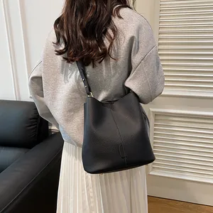 Minimalist black bucket bag with lychee texture and adjustable strap on a model