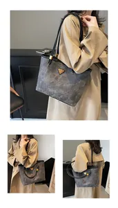 Detail of grey textured tote bag featuring black long handles and golden metal hardware