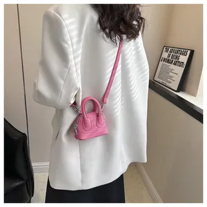 Nahaufnahme einer rosa Mini-Umhängetasche mit Litchi-Struktur am Model im Sonnenlicht