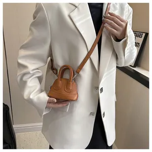 Detail einer mini braunen Umhängetasche aus Leder auf einem weißen Blazer
