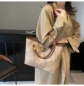 Detail of large beige tote bag with marble pattern, brown leather straps and triangle logo