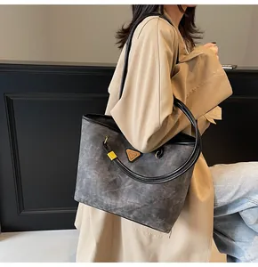 Detail of grey suede tote bag with golden metal triangle logo worn by model in beige coat