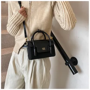 Detail of a black textured crossbody bag with golden hardware and brand lettering