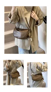 Detail view of a brown leather half-moon crossbody bag with cute teddy bear charm