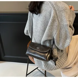 Détail d'un sac bandoulière vintage en cuir noir avec logo métallique et breloque éléphant