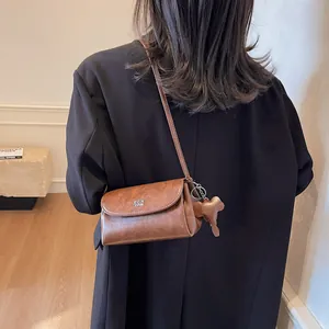 Sac bandoulière vintage caramel avec breloque éléphant porté par un mannequin élégant