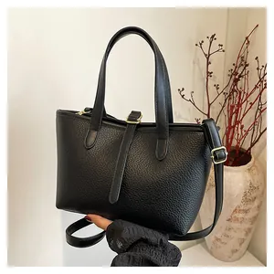 Detail of black lychee grain leather tote bag with gold hardware held by a model