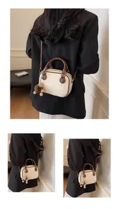 Detail view of mini Boston bag in cream and brown with detachable strap and plush pendant