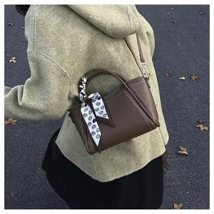 Detail of brown bucket bag with white stitching and heart pattern scarf on handle