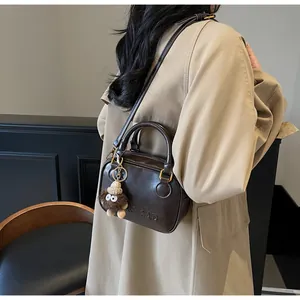 Detail of dark brown retro crossbody bag with embossed letters and plush charm