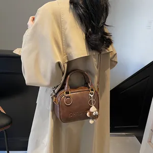 Retro dark brown Boston handbag with gold hardware and plush charm on a trench coat model