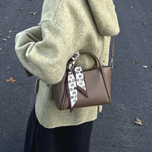 Brown bucket bag with scarf-wrapped handle and contrast stitching on green coat background